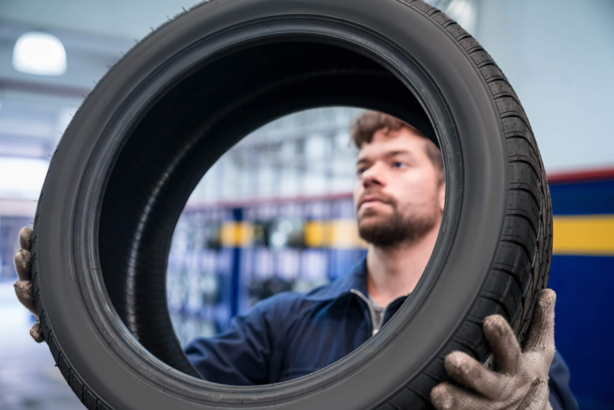 Young apprentice holding car wheel in the auto repair shop. Close-up of tire and face.
