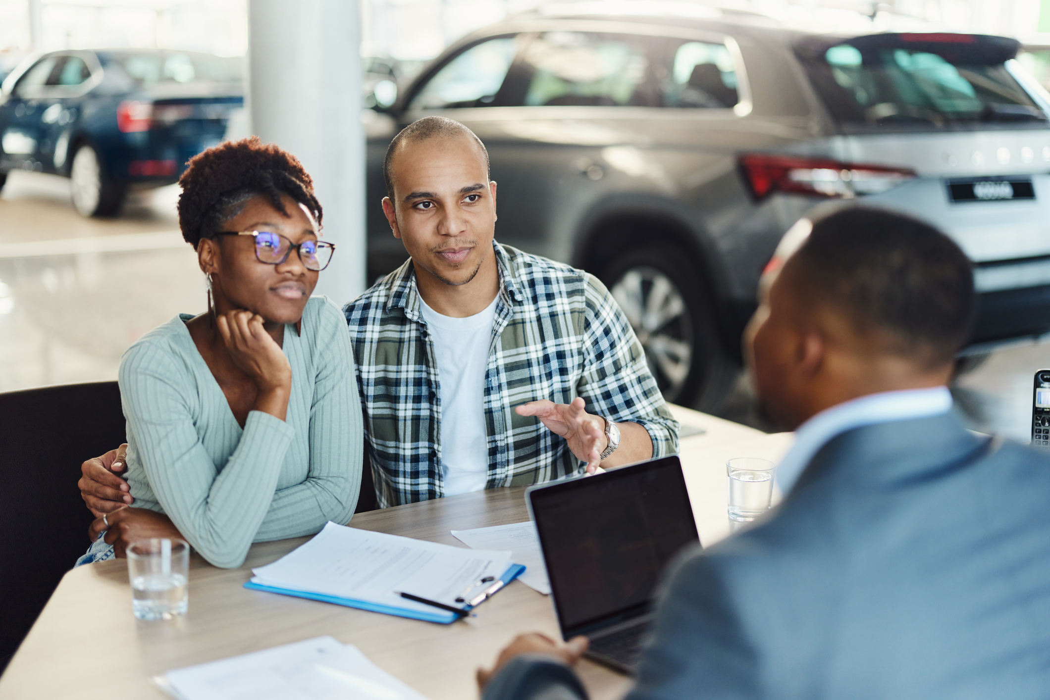 Young diverse couple communicating with a car salesman on a meeting in showroom. Focus is on man.