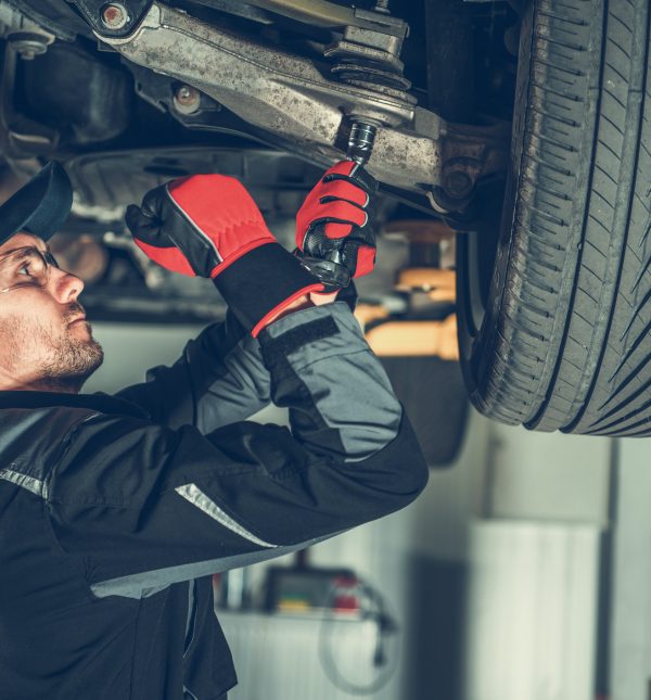 Caucasian Car Mechanic Adjusting Tension in Vehicle Suspension Element. Professional Automotive Service.