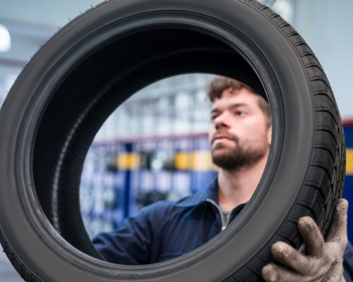 Young apprentice holding car wheel in the auto repair shop. Close-up of tire and face.