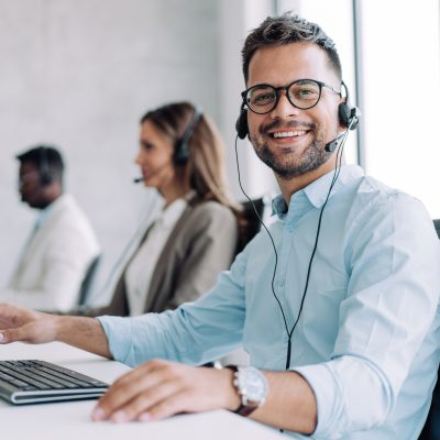 Shot of call center operators working in the office. Call center agent working with his colleagues in modern office. Smiling handsome businessman working in call center.