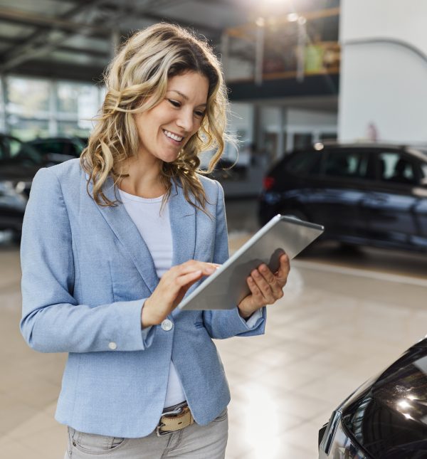 Happy female salesperson working on touchpad in a car showroom.