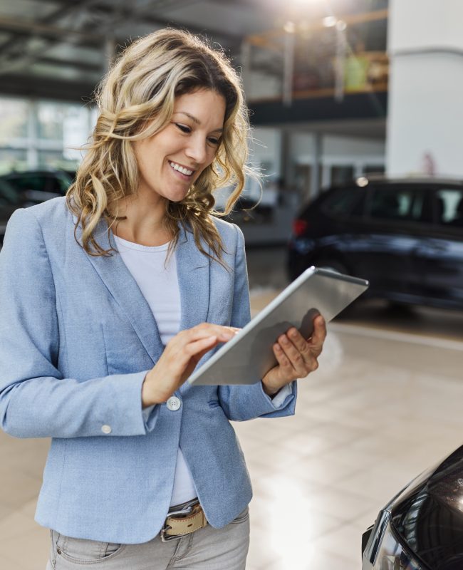 Happy female salesperson working on touchpad in a car showroom.