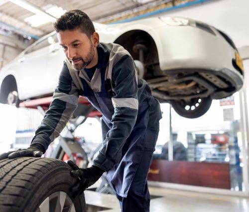 Happy Latin American mechanic changing a flat tire on a car at an auto repair shop