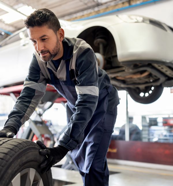 Happy Latin American mechanic changing a flat tire on a car at an auto repair shop