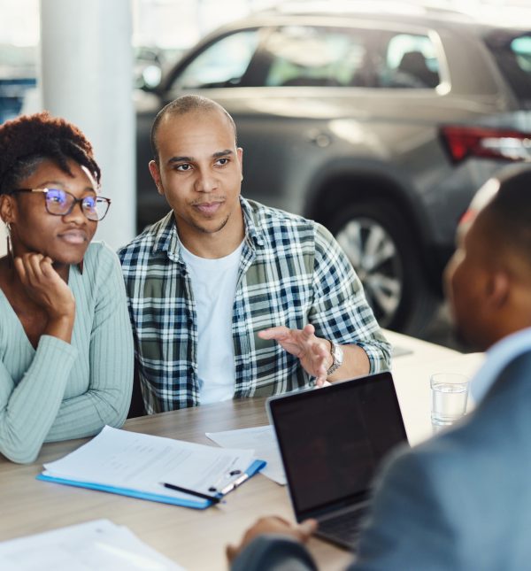 Young diverse couple communicating with a car salesman on a meeting in showroom. Focus is on man.
